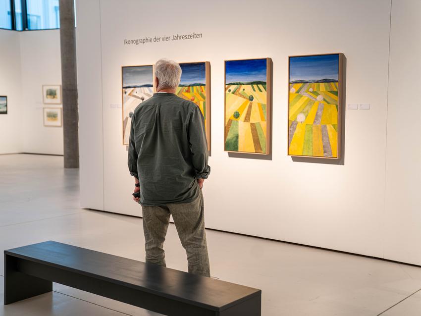 Ein Mann steht in der Ausstellung "Harro Pirch. Eine Annäherung in Bildern und sieht sich die Werke der vier Jahreszeiten, 2024 von Harro Pirch an.
